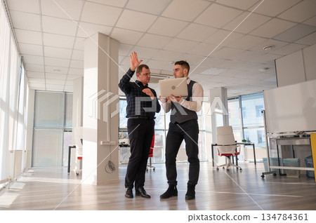 Two Caucasian men looking at a laptop and discussing work.  134784361