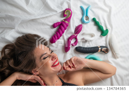 A beautiful Caucasian woman in black lingerie lies among sex toys. A beautiful Caucasian woman in black lingerie lies among sex toys. 134784365
