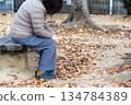 A middle-aged woman sitting alone on a bench in an autumn park A middle-aged woman sitting alone on a bench in an autumn park 134784389