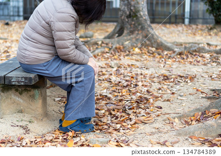 秋日公園裡，一位中年婦女獨自坐在長椅上。 134784389