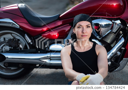 Brunette woman repairs a red motorcycle.  134784424