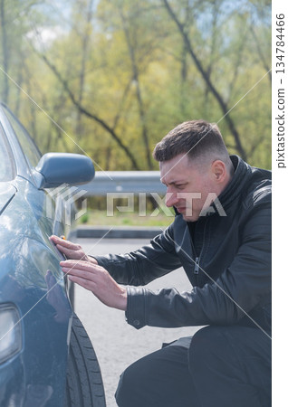 Caucasian man examines defects on his car body.  134784466