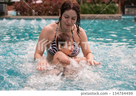 Caucasian woman holds her son while swimming in a pool on vacation. Mom teaches little boy to swim. Caucasian woman holds her son while swimming in a pool on vacation. Mom teaches little boy to swim. 134784499