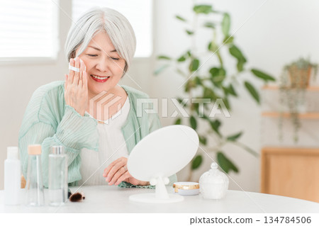 一位微笑的老婦人正在塗抹粉底、蜜粉和化妝品。 一位微笑的老婦人正在塗抹粉底、蜜粉和化妝品。 134784506
