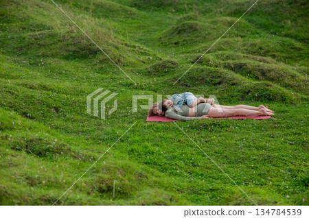 Caucasian woman doing yoga with her little son outdoors.  134784539