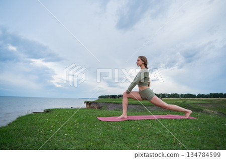 Caucasian woman doing yoga on the river bank. Warrior pose. 134784599