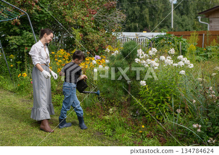 Caucasian woman and her son watering flowers in the garden. Caucasian woman and her son watering flowers in the garden. 134784624