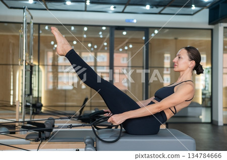 Caucasian woman doing exercises on reformer machine. Caucasian woman doing exercises on reformer machine. 134784666