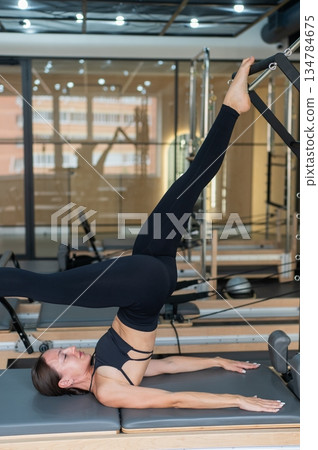 Caucasian woman doing leg exercise on reformer machine.  134784675