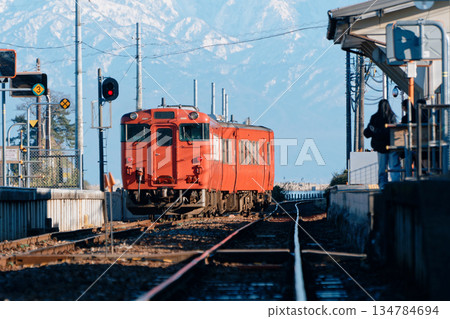 一列橘色的本地火車駛過某個地點，朝著雪山方向駛去，人們正在送別它。 134784694