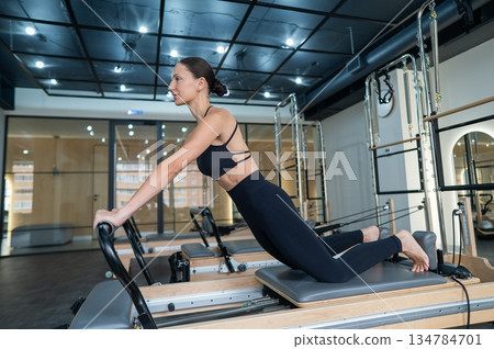 Caucasian woman doing exercises on reformer machine. Caucasian woman doing exercises on reformer machine. 134784701
