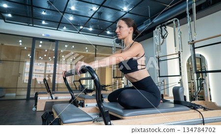 Caucasian woman doing exercises on reformer machine. Caucasian woman doing exercises on reformer machine. 134784702