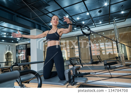 Caucasian woman doing exercises on reformer machine. Caucasian woman doing exercises on reformer machine. 134784708