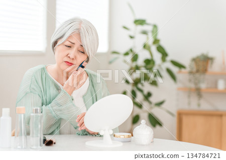 Senior woman applying foundation, powder, and makeup (worries, skin troubles, skin problems) 134784721