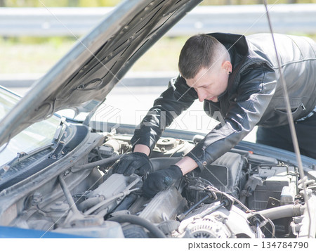 A man changes spark plugs in his car.  134784790
