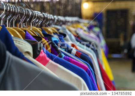 Colorful variety of vintage apparel and second-hand clothes hanging on a rack in a thrift shop or flea market. This image captures the concept of sustainable fashion, retro style, and the treasure 134785892