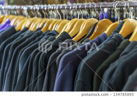 Colorful variety of vintage apparel and second-hand clothes hanging on a rack in a thrift shop or flea market. This image captures the concept of sustainable fashion, retro style, and the treasure 134785893