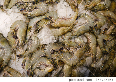 Fresh shrimps displayed on ice at a seafood market during early morning hours, showcasing their vibrant colors and textures ready for purchase or cooking 134786763