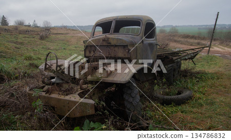 dilapidated vintage truck sits in misty meadow, bent grille and exposed engine, flat tires partially sunk into 134786832