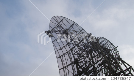 mesh dragonfly sculpture towering against sky metal lattice wings and industrial frame, cloudy atmosphere, 134786847