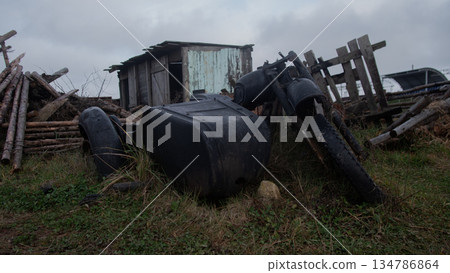 abandoned farm machinery and tanks near shed, rusted tires and toppled barrels, collapsed wooden fence 134786864