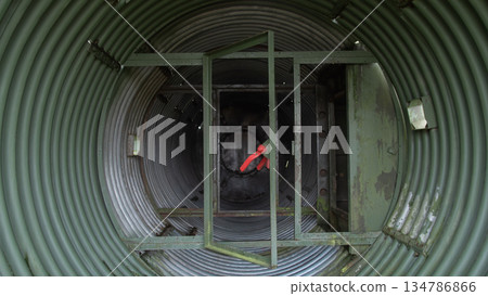 inspector inside corrugated metal tunnel performing maintenance inspection, clad in red jacket and helmet, inspector inside corrugated metal tunnel performing maintenance inspection, clad in red jacket and helmet, 134786866