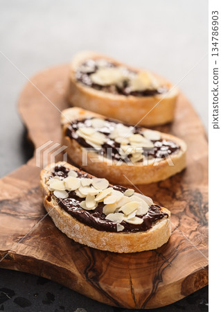 Rustic ciabatta with organic chocolate cream and almond flakes on olive wood board Rustic ciabatta with organic chocolate cream and almond flakes on olive wood board 134786903