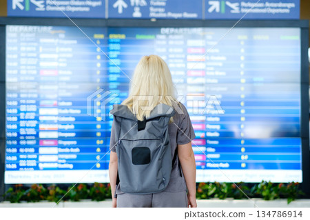 Traveling to new destinations as a woman checks the departure board at an airport, planning her next journey on a summer Thursday in July Traveling to new destinations as a woman checks the departure board at an airport, planning her next journey on a summer Thursday in July 134786914