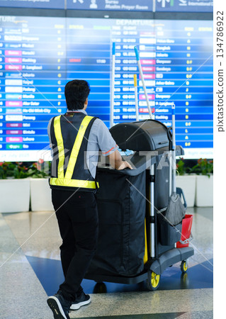 Janitor cleaning airport terminal while flight information displays are updated, showcasing the busy environment Janitor cleaning airport terminal while flight information displays are updated, showcasing the busy environment 134786922