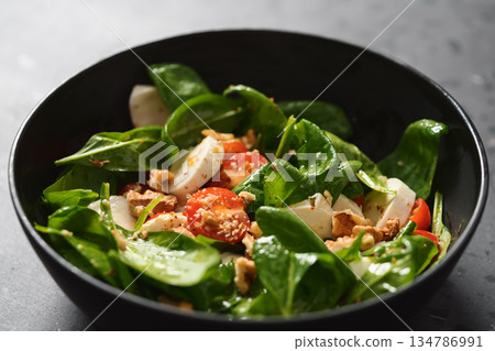 Salad with spinach, tomatoes and mozzarella in black bowl on concrete countertop 134786991