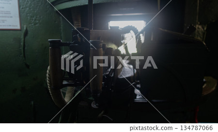 dimly lit engine room interior showing rusted generator, tangle of pipes and valves backlit by narrow window 134787066