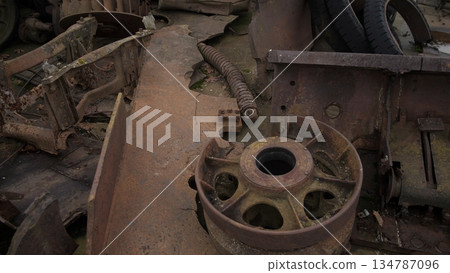 rusted tank wheel and chassis exposed, corroded metal, flaking paint, scattered debris, silent salvage site, overcast light, heavy patina and pitted surfaces, ideal for editorial features or texture 134787096