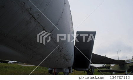 wide underside perspective showing open ventral bay and cargo ramp silhouette, dark interior throat contrasted with gray skin and landing gear struts, cloudy sky and damp ground conveying maintenance 134787113