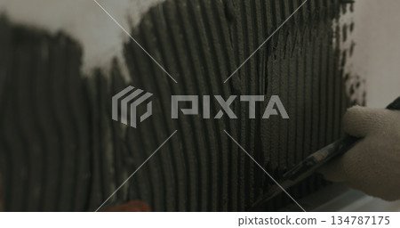 closeup worker applying concrete glue to wall before applying brick tile closeup worker applying concrete glue to wall before applying brick tile 134787175