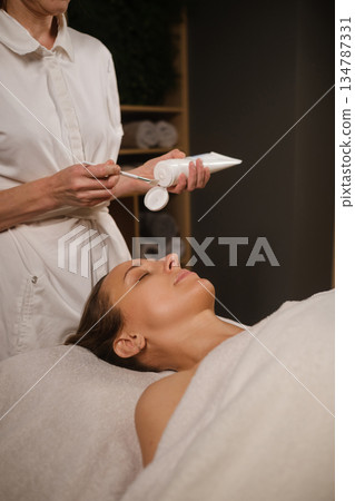 The master holds a face cream in his hands. Relaxation session at the spa with facial treatment for women 134787331