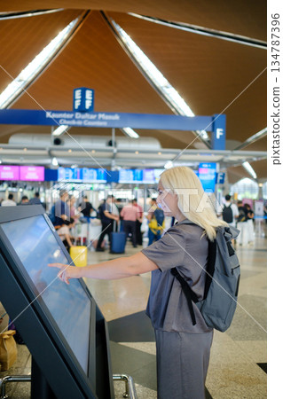 Young traveler using a digital information kiosk at an airport to navigate and find her way during peak travel hours Young traveler using a digital information kiosk at an airport to navigate and find her way during peak travel hours 134787396