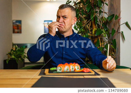 Man makes a funny expression with chopsticks while sitting before a sushi plate. Man makes a funny expression with chopsticks while sitting before a sushi plate. 134789080