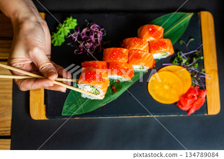 Close-up of a hand lifting a salmon sushi piece from a stylish serving board. 134789084