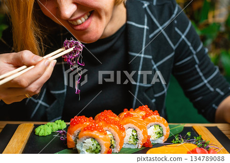 Tight shot of a woman holding chopsticks over a vibrant sushi assortment. 134789088