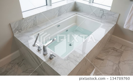 Modern luxury bathroom corner soaking tub with marble surround and chrome fixtures filled with water 134789760