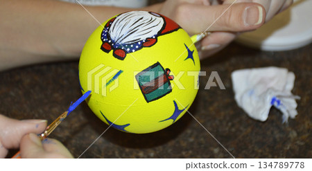 Female hands carefully painting a Christmas ball in vibrant orange hues Female hands carefully painting a Christmas ball in vibrant orange hues 134789778