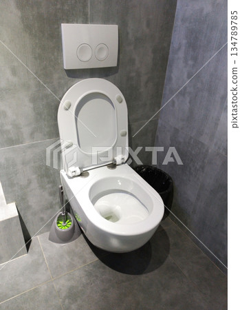 A modern wall-hung toilet with an open lid installed in a gray-tiled bathroom 134789785