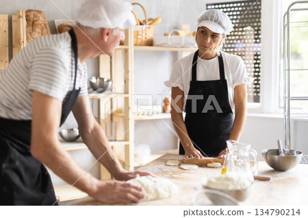 Two bakers prepare dough for baking - shaping it and rolling it out with rolling pin Two bakers prepare dough for baking - shaping it and rolling it out with rolling pin 134790214