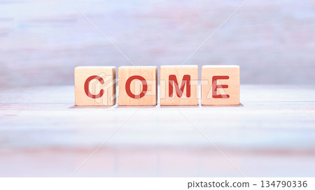 Four wooden blocks each display a letter together they spell COME in vibrant red against a pale, painted backdrop, conveying an invitation Four wooden blocks each display a letter together they spell COME in vibrant red against a pale, painted backdrop, conveying an invitation 134790336
