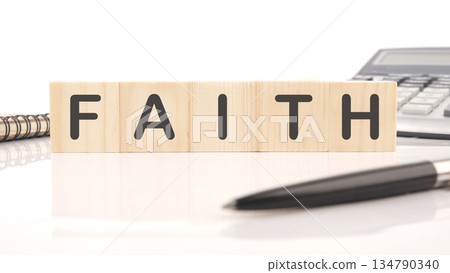 The word Faith is prominently spelled out using wooden blocks on a white surface. A pen, notebook, and calculator are also present The word Faith is prominently spelled out using wooden blocks on a white surface. A pen, notebook, and calculator are also present 134790340