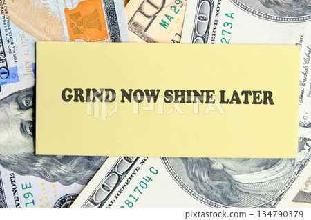 A light yellow card with the phrase GRIND NOW SHINE LATER rests atop a bed of United States currency, suggesting hard work can lead to future success A light yellow card with the phrase GRIND NOW SHINE LATER rests atop a bed of United States currency, suggesting hard work can lead to future success 134790379