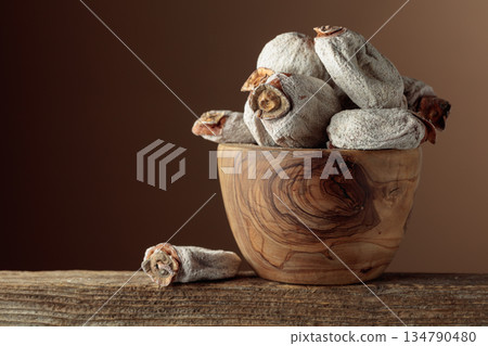 Dried persimmons in a wooden dish on a brown background. Dried persimmons in a wooden dish on a brown background. 134790480