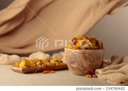 Yellow sultana raisins in a wooden bowl on a beige background. Yellow sultana raisins in a wooden bowl on a beige background. 134790482