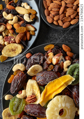 Dried tropical fruits, nuts, and raisins in black plate. Dried tropical fruits, nuts, and raisins in black plate. 134790625