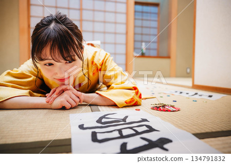 A young woman in a kimono lies down in a Japanese-style room with her calligraphy work on the floor A young woman in a kimono lies down in a Japanese-style room with her calligraphy work on the floor 134791832